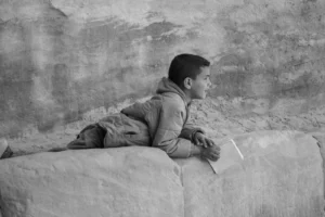 Black and white image of a child holding a piece of paper, laying on the ground
