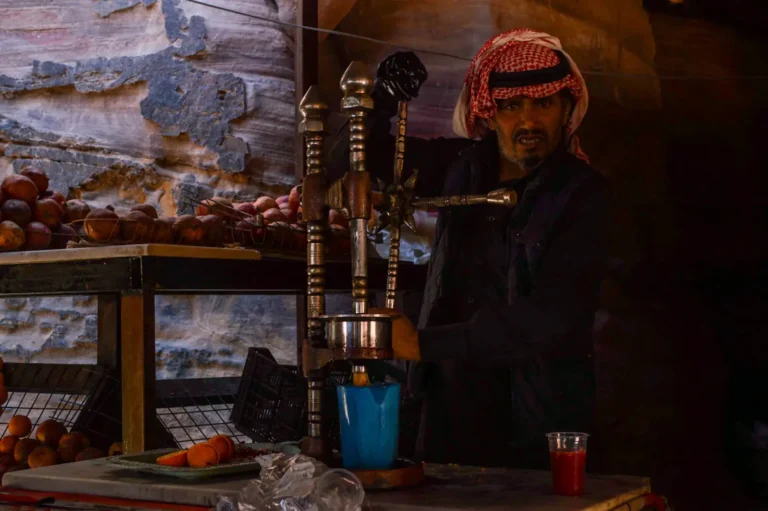 Arab old man making orange juice using a traditional machine who is looking straight in the camera